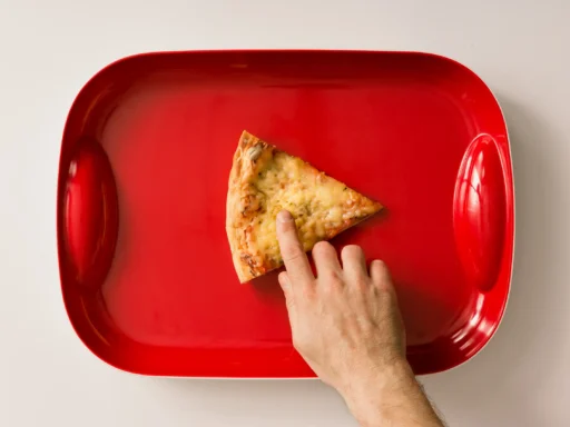 Finger touching a pizza slice on a red tray, imitating the youtube play button, symbolising notebooklm's repurposing capabilities.